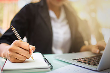 person taking notes in front of laptop person taking notes in front of laptop